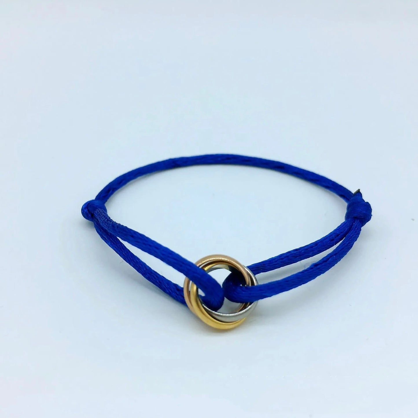 Adjustable blue cord bracelet featuring a tricolor gold and silver interlocking ring charm. Friendship or stacking jewelry.
