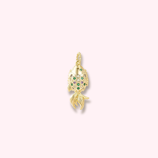 Gold fish-shaped charm pendant, intricately adorned with small colorful gems (green, purple, and white), featuring a shiny finish, against a soft pinkish-white background.