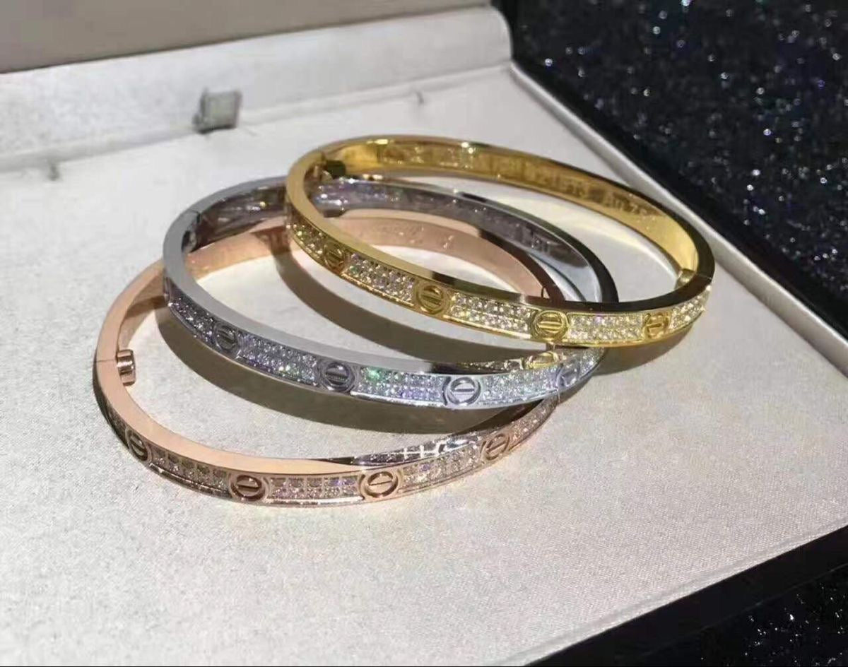 Set of three thin 'Love' bracelets in gold, rose gold, and silver tones, featuring pavé simulated diamonds. Elegant stackable bangles.