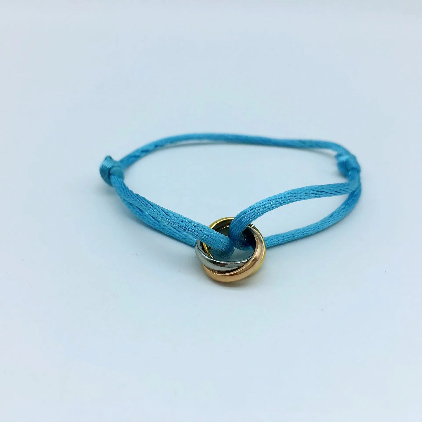 Adjustable pink cord bracelet featuring a tricolor gold and silver interlocking ring charm. Perfect friendship or stacking accessory.